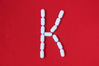 Kırmızı arka planda haplardan oluşan alfabe. Uyuşturucunun alfabesi. K harfi haplardan yapılmış. İlaçların büyük harfi K
