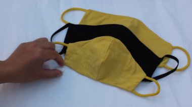 Siyah ve sarı tıbbi maske ve elle sayım hapları. Koronavirüsten korunma. Bir kadın beyaz arka planda beyaz bir maskenin yanında beyaz haplar sayıyor. Yakın plan.
