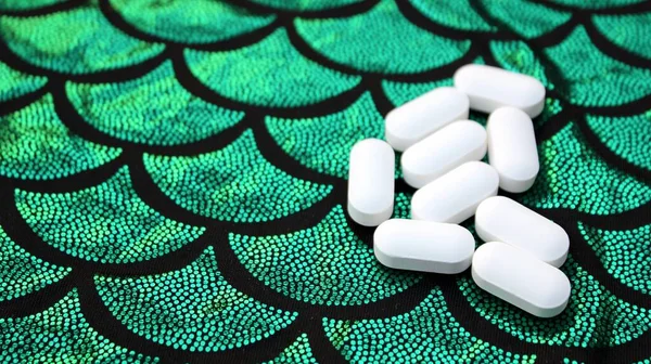 A handful of white pills on a black-green background imitating scales. Calcium tablets in a shiny background.