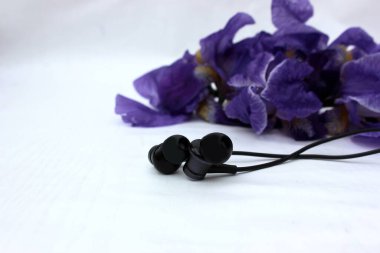 Siyah kulaklıklar arka plandaki çiçeklerde beyaz renkte izole edilmiş. Beyaz üzerine izole edilmiş mavi iris çiçeklerinin arka planında siyah kulaklık. Yan görünüm, kopyalanma alanı