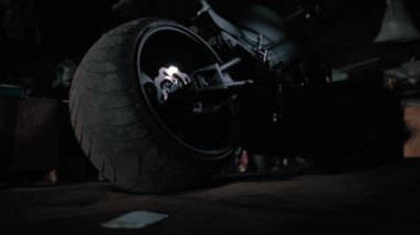 Gece vakti garajda büyük tekerlekli siyah bir motosiklet vardı.