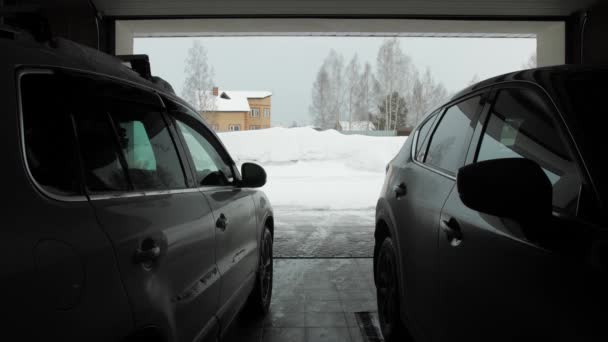 De mens reinigt sneeuw met een sneeuwgooier. Uitzicht vanaf twee auto 's vanuit garage — Stockvideo