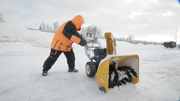 Чоловік вмикає снігоприбиральник взимку в помаранчевій куртці — стокове відео