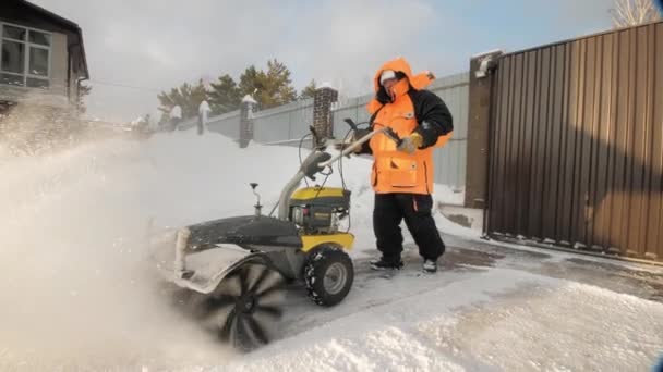 El hombre limpia la nieve en el patio con una barredora en el invierno — Vídeo de stock