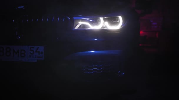 TOMSK, RUSSIA - 26 de julho de 2019: Vista óptica BMW Série 7 através de fumaça, fundo preto. Iluminação colorida. Adaptiver LED — Vídeo de Stock