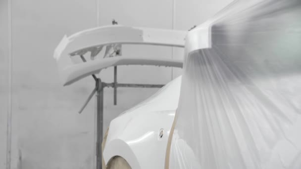 A fehér autó egy átlátszó filmmel borított permetező fülkében áll. Festésre kész — Stock videók