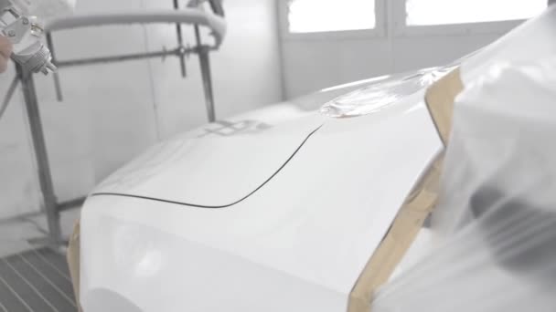 Egy fehér autó kifestésének folyamata egy permetező fülkében. Egy férfi szórópisztollyal. — Stock videók