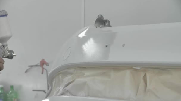 Proces malowania zderzaka białego samochodu w kabinie lakierniczej. Mężczyzna używający pistoletu natryskowego — Wideo stockowe