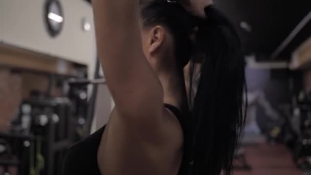 Athletic sexy girl in gym collects hair in a bun so as not to interfere — Stock Video