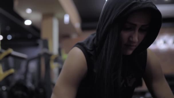 Athlétique fille sexy écouter de la musique tout en étant assis sur un banc dans un t-shirt avec une capuche dans la salle de gym — Video