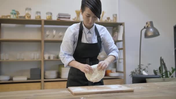 Stylish girl in a black apron kneads the dough on a wooden cutting board — Stock Video