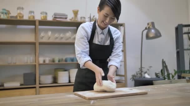Stylish girl in a black apron kneads the dough on a wooden cutting board — Stock Video