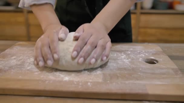 Girl in a black apron kneads the dough on a wooden cutting board close up — Stock Video