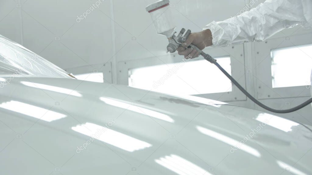 Process of painting a white car in a spray booth. Man using a spray gun
