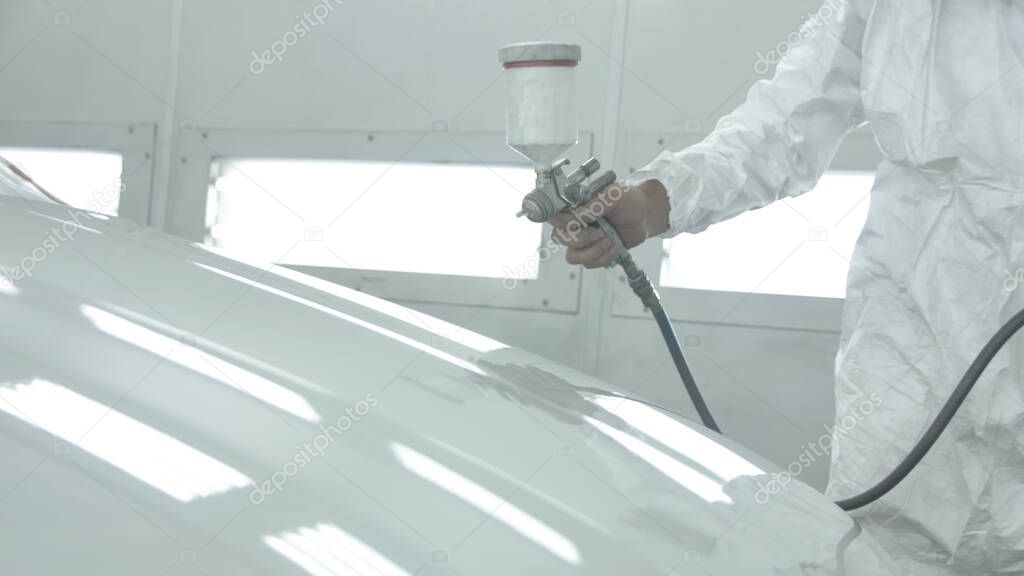 Process of painting a white car in a spray booth. Man using a spray gun