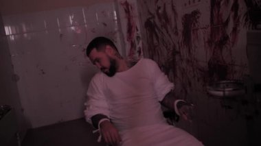Deli gömleği giymiş deli bir adam sandalyeye bağlanmış, duvarları kanlı bir odada aşırı doz almış katil bir psikopat.
