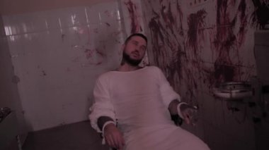 Deli gömleği giymiş deli bir adam sandalyeye bağlanmış, duvarları kanlı bir odada aşırı doz almış katil bir psikopat.