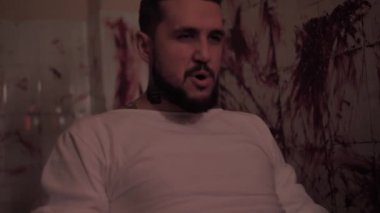 Deli gömleği giymiş deli bir adam sandalyeye bağlanmış, kanlı duvarlı bir odada katil bir psikopat.