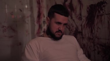 Deli gömleği giymiş deli bir adam sandalyeye bağlanmış, kanlı duvarlı bir odada katil bir psikopat.