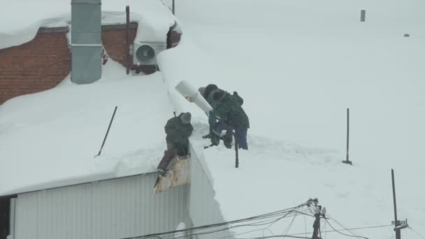 Tre personer kastar snö från taket — Stockvideo