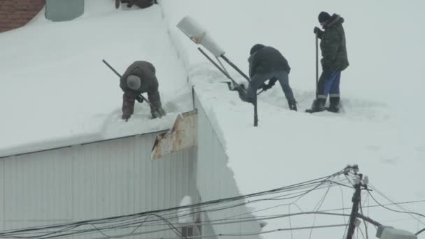 Tre personer kastar snö från taket — Stockvideo