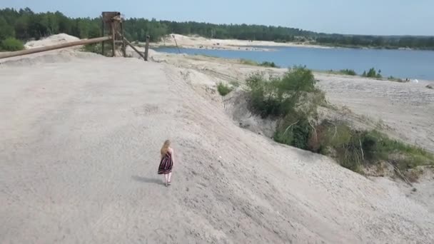 Chica en un vestido de sol camina a lo largo del borde de un pozo de arena — Vídeo de stock