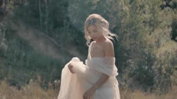 Blonde girl in a white dress sitting near the lake — Stock Video