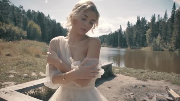 Chica rubia en un vestido blanco sentado cerca del lago — Vídeo de stock