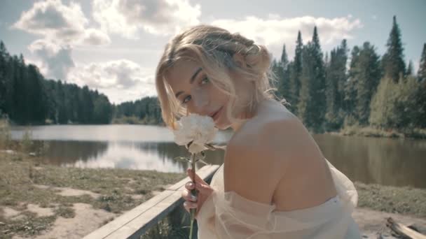 Blondýny dívka v bílých šatech sedí v blízkosti jezera — Stock video