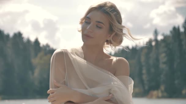 Chica rubia en un vestido blanco sentado cerca del lago — Vídeo de stock
