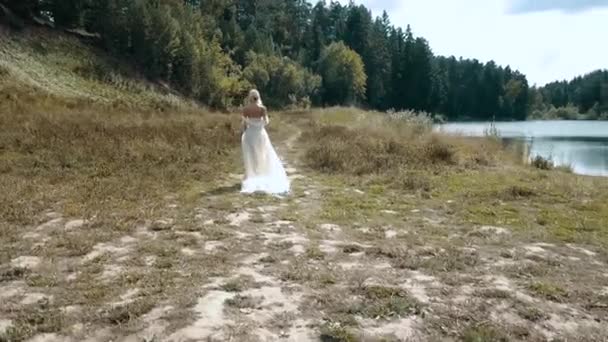 Девушка идет через лес и тянет белое платье на землю — стоковое видео