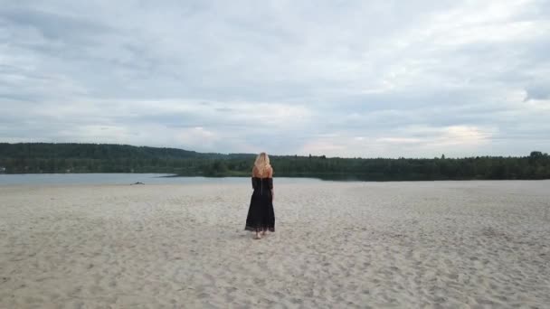 Mujer rubia con vestido negro en la playa de arena — Vídeos de Stock