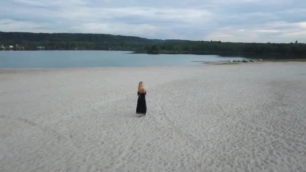 Блондинка в черном платье на песчаном пляже — стоковое видео