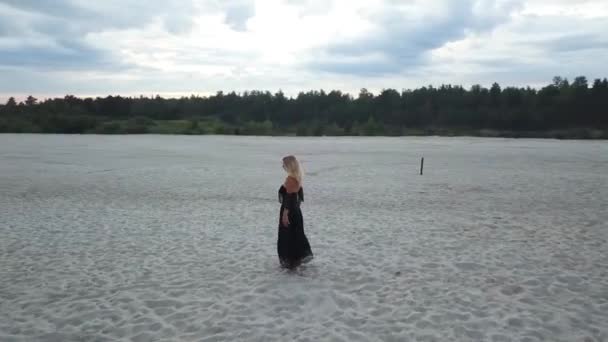 Mujer rubia con vestido negro en la playa de arena — Vídeo de stock