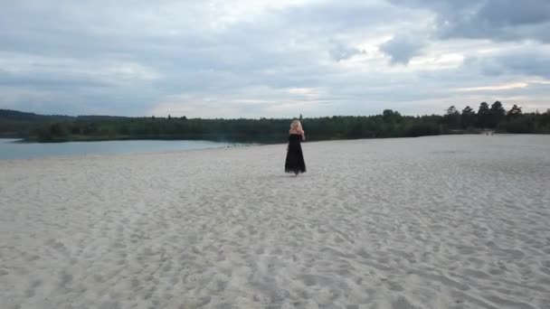 Блондинка з чорною сукнею на піщаному пляжі — стокове відео