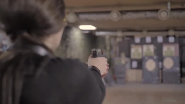Flicka i svarta kläder tar fram en pistol från ett hölster och skjuter — Stockvideo