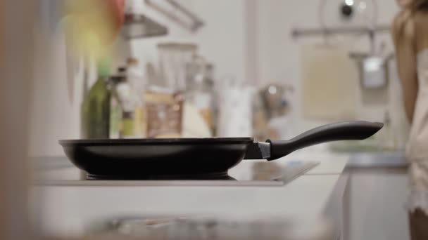 Pan on the stove, a girl in pajamas washes dishes in the background — Stock Video