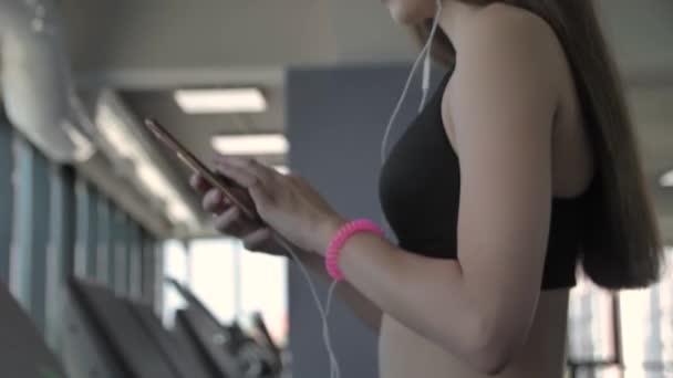 Vacker sportig tjej lyssnar på musik från smartphone med appen igång på löpbandet — Stockvideo