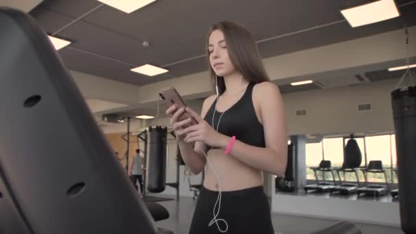 Mooi sportief meisje luisteren naar muziek van smartphone met app draait op loopband — Stockvideo