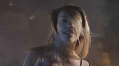 Siyah iç çamaşırlı, tuğladan duvarlı, renkli ışıklı güzel bir sarışın.