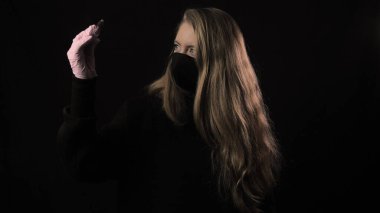 Siyah maskeli kız üzerinde kan olan bir test tüpü ve Covid-19 yazısını tutuyor. Siyah arka planda izole edilmiş. Sağlık ve tıbbi konsept. Koronavirüs salgını