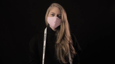 Pembe maskeli kız üzerinde covid-19 yazan bir kaset tutuyor. Siyah arka planda izole edilmiş. Sağlık ve tıbbi konsept. Portreyi kapat. 4 bin. Coronavirus Salgını, Hastalık, Salgın