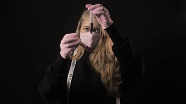 Pembe maskeli bir kız, üzerinde kan olan bir test tüpü tutuyor ve yazıtlar kabartma 19 ve maskeyi büküyor. Siyah arka planda izole edilmiş. Sağlık ve tıbbi konsept. Koronavirüs salgını