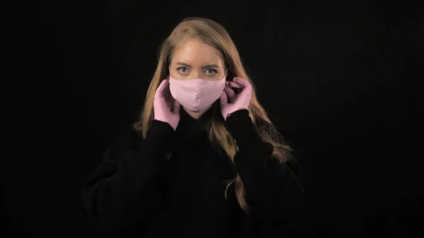 Altın saçlı genç bir kadın pembe bir tıbbi maske takıyor. Siyah arka planda izole edilmiş. Sağlık ve tıbbi konsept. Portreyi kapat. 4 bin. Coronavirus Salgını, Hastalık, Salgın