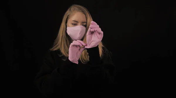 Fille en rose masque médical redresse gants roses sur la main. Isolé sur fond noir. Soins de santé et concept médical. Gros plan portrait. 4k. Coronavirus Épidémie, maladie, pandémie — Photo