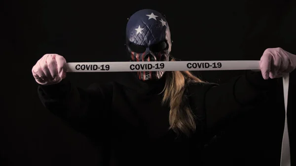 Chica en la máscara de miedo sostiene una cinta blanca con la inscripción covid 19. Aislado sobre fondo negro. Salud y concepto médico. Epidemia de Coronavirus, enfermedad, pandemia. Estados Unidos Máscara — Foto de Stock