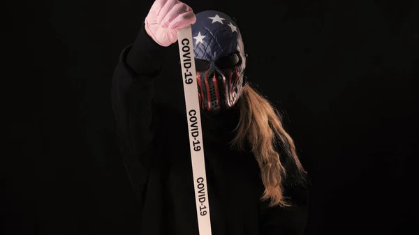 Chica en la máscara de miedo sostiene una cinta blanca con la inscripción covid 19. Aislado sobre fondo negro. Salud y concepto médico. Epidemia de Coronavirus, enfermedad, pandemia. Estados Unidos Máscara — Foto de Stock