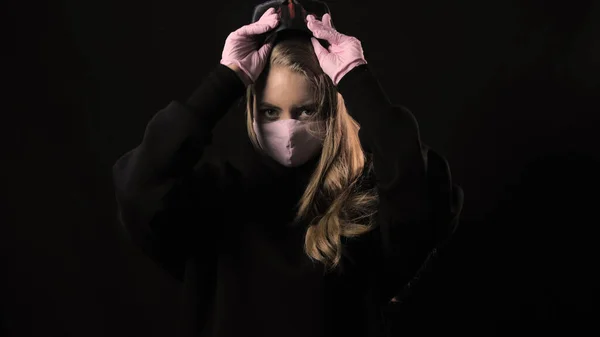 Mädchen zieht eine gruselige USA-Maske aus und darunter liegt eine rosafarbene medizinische Maske. Vereinzelt auf schwarzem Hintergrund. Gesundheitsfürsorge und medizinisches Konzept. Porträt aus nächster Nähe. 4k. Coronavirus Epidemie, Krankheit, Pandemie — Stockfoto