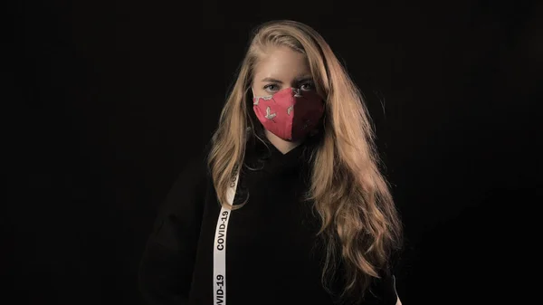 Beyaz kurdeleli ve Covid 19 yazılı kız kırmızı bir maske takıyor. Siyah arka planda izole edilmiş. Sağlık ve tıbbi konsept. Koronavirüs salgını