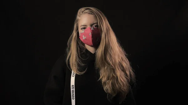 Girl with a white ribbon and the inscription covid 19 puts on a red fun mask. Isolated on black background. Health care and medical concept. Coronavirus Epidemic — Stock Photo, Image